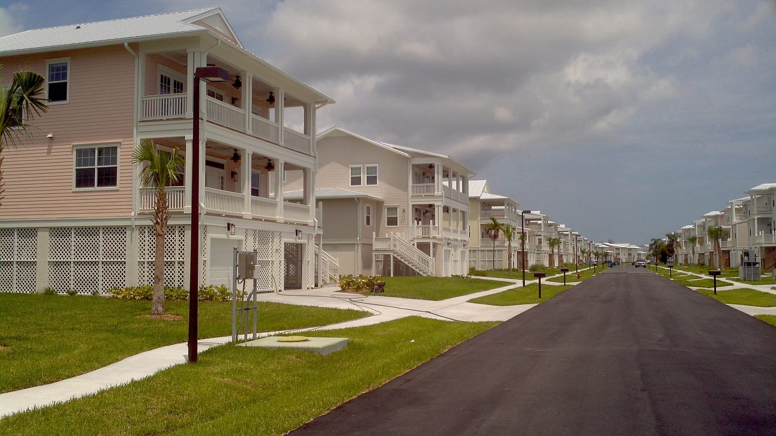 Two-story Navy family homes with double porches along a residential street at Naval Air Station Key West, with palm trees and an overcast sky