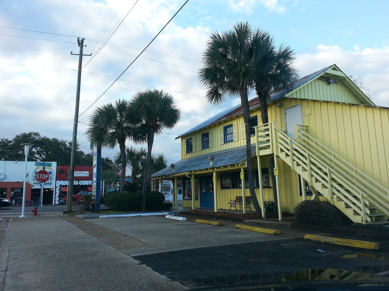 Two story yellow commercial building with palm trees beside a street sign reading Miracle Strip in Fort Walton Beach, Florida