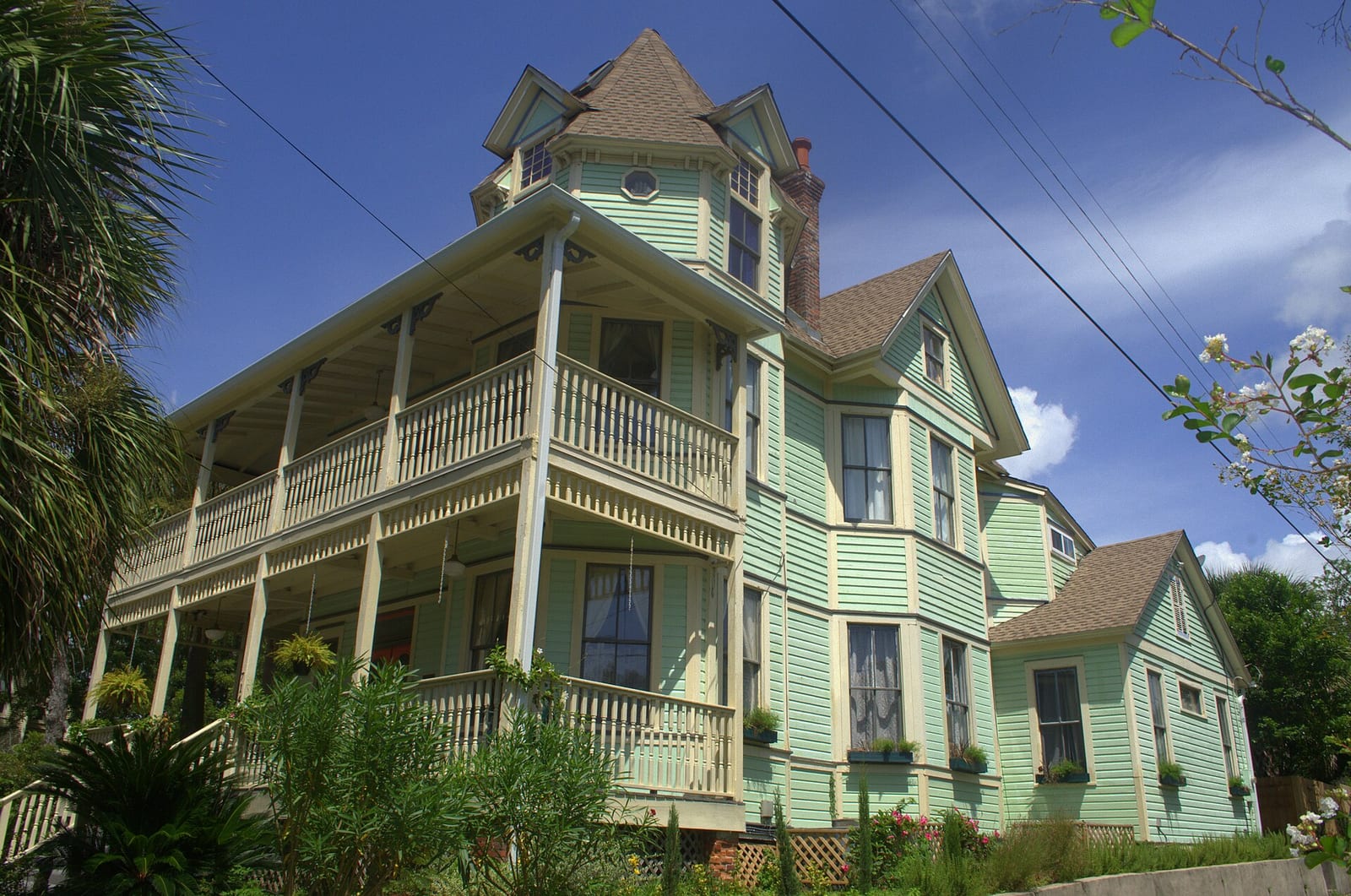 Three-story green Victorian house with wraparound double porches and a corner tower under a blue sky in Pensacola, Florida