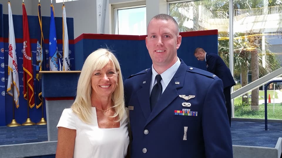 An Air Force officer in service dress at a ceremony with flags behind
