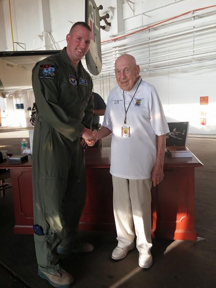 Gregg Costin in a flight suit shaking hands with a veteran inside a hangar