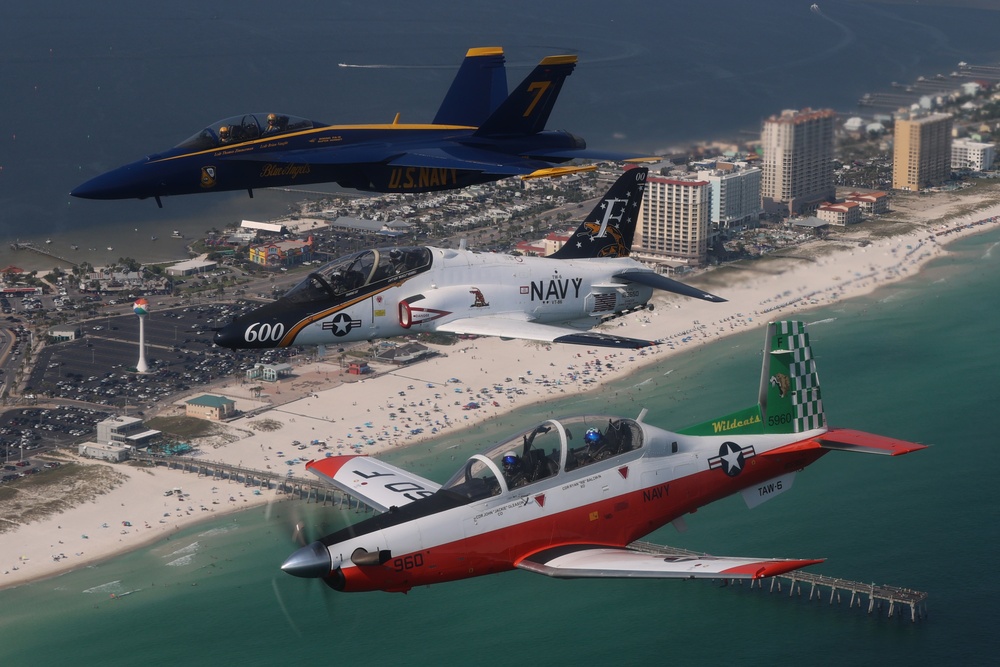 A T-6A, T-45C and Blue Angels F/A-18F flying in formation beside Pensacola Beach in July 2023