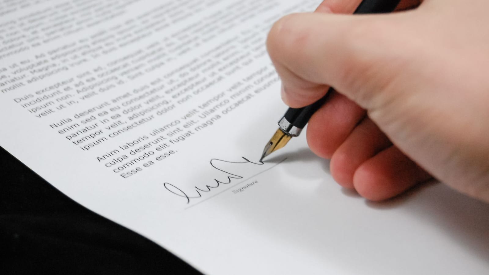 Close-up of a hand signing a printed document at a signature line with a black fountain pen